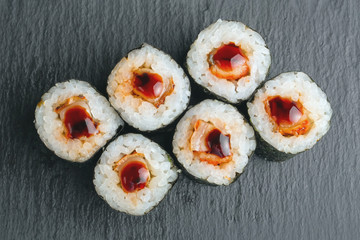 Sushi Rolls with salmon and rice inside wrapped in nori leaf and poured drops of soy sauce on black slate