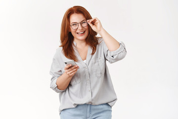 Never was easier. Cheerful carefree happy emotive redhead middle-aged woman checking glasses hold smartphone laughing pleased joyful camera get used new phone managing schedule via cellphone