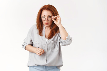 Confused stunned speechless redhead middle-aged woman taking off glasses stare sideways astonished puzzled cannot understand what going on strange things happen standing perplexed white wall