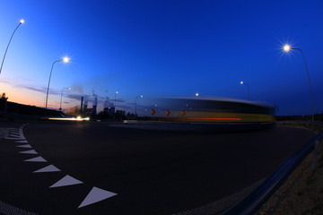 Fototapeta na wymiar Smugi świateł samochodów na rondzie w nocy po zachodzie słońca, most, elektrownia, błękitne niebo.