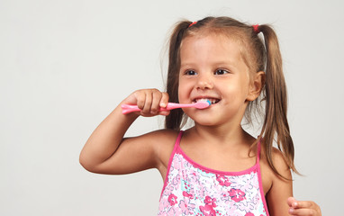 Little girl brushing teeth with toothbrush over white background with copy space