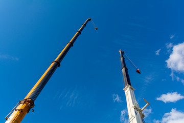 Two boom truck cranes. Raised arrow of a truck crane against the sky.