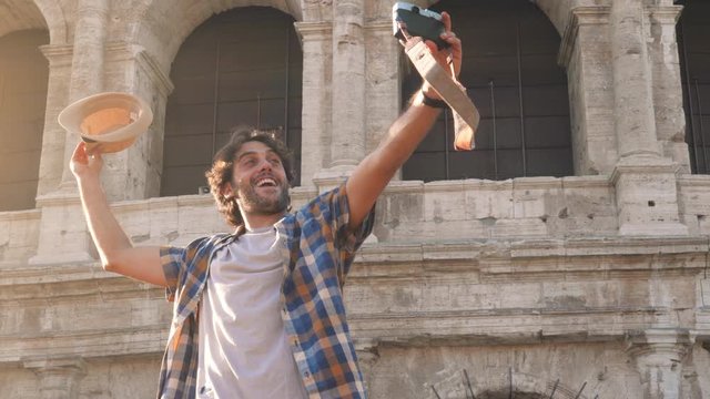 Happy young man tourist with bike wearing shirt tanding on a column taking funny pictures and selfies at colosseum in Rome, Italy at sunrise.