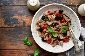 Whole wheat pasta fusilli with tuna, tomato and black olives. Top view with copy space.