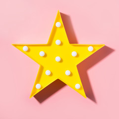 Yellow lamp as star with white LED lights with shadow on pastel pink background. Creative minimal concept. Top view. Flat lay style. Children's modern night light. Square image.