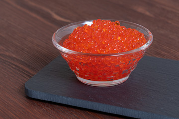 Red caviar in the glass jar on the dark brown wooden background
