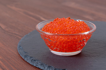 Red caviar in the glass jar on the dark brown wooden background