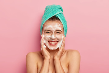 Pampering and hygiene concept. Happy young European woman massages cheeks, aplies bubble foam,...