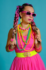 Lovely girl with a multi-colored braids hairstyle and bright make-up, posing in studio against a blue background, holding a lollipop in her hand.