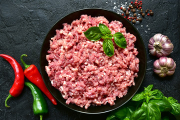 Homemade minced meat in a black bowl over dark slate, stone or concrete background with ingredients for making.Top view with copy space.