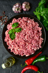 Homemade minced meat in a black bowl over dark slate, stone or concrete background with ingredients for making.Top view with copy space.
