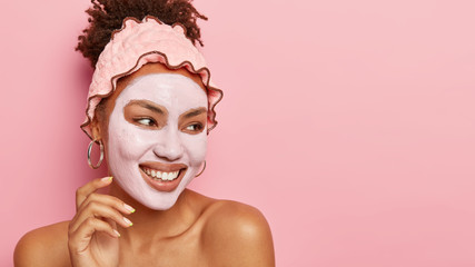 Smiling charming young woman cares about skin, applies clay mask, nourishes complexion with...