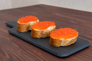 Set of three sandwiches with red caviar on the grey stone background