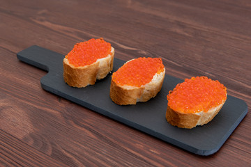 Set of three sandwiches with red caviar on the grey stone background