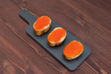 Set of three sandwiches with red caviar on the grey stone background