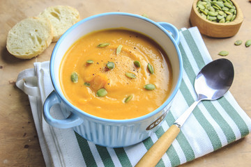 Pumpkin soup and organic pumpkins on rustic table.