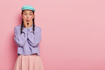 Photo of emotional Asian woman with stunning look, forgets about something important, looks away on free space, dressed in stylish clothes, poses over pink wall. People, face expressions, reaction
