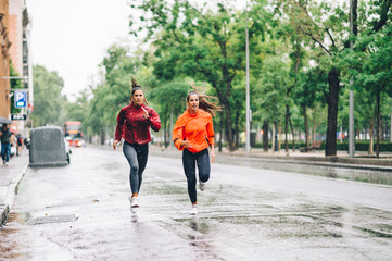 Two beautiful women running in city with rain and puddles.
