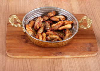 Service of fried chicken in animal oil in a copper bowl from a close angle on a wooden table