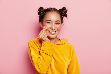 Portrait of happy Asian lady with pleasant smile on face, makes like sign, shapes heart with...