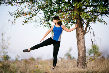 Fit woman runner doing warming-up exercises, preparing for morning workout in the park. Street fitness, sport, exercising, people and healthy lifestyle concept