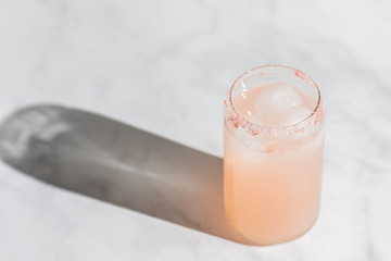 A strawberry lemonade drink in a can like glass standing on a marble countertop. Direct sunlight from the aide casting a hard shadow on the countertop. Light pink refreshing drink during summer. 