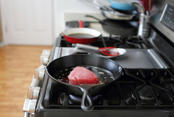  Ahi tuna steak searing in a cast iron skillet on a gas stove.