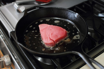  Ahi tuna steak searing in a cast iron skillet on a gas stove.