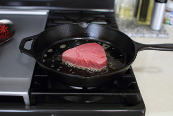  Ahi tuna steak searing in a cast iron skillet on a gas stove.