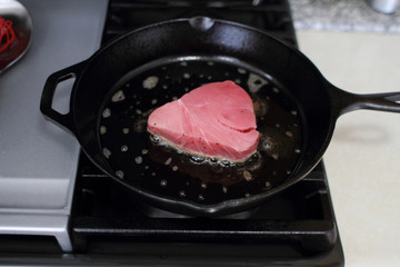  Ahi tuna steak searing in a cast iron skillet on a gas stove.
