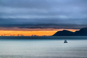 Scenery of a small ship on the Bering sea and the St Lawrence island in the background at dusk on a...