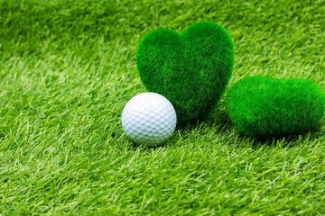 Golf ball and green grass heart shape are on green grass.
