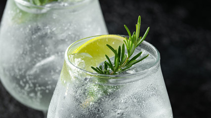 Gin and Tonic Alcohol drink with Lime, Rosemary and ice on rustic black table - obrazy, fototapety, plakaty
