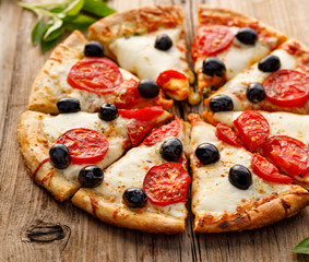 Pizza with mozzarella cheese, tomatoes and  black olives,  cut into pieces on a wooden  background, close up. Italian food