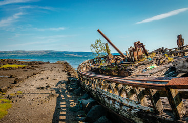 Beautiful seascape with a semi-destroyed old fishing boat in the beach and the Sound of Mull in the background. Isle of Mull, Scotland, August 2019.