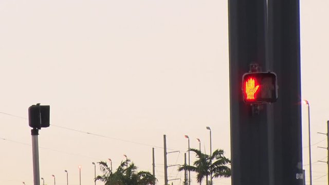 A Red Don't Walk Signal With Hand Up Indicates Caution To Pedestrians As Cars Drive By In The Foreground At A Traffic Intersection With Light Poles, Power Lines And Gray Sky In The Background.