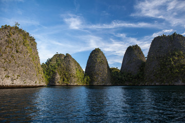 Fototapeta na wymiar Dramatic rock islands rise from the tranquil seascape amid the remote, tropical islands of Raja Ampat, Indonesia. This equatorial region is possibly the center for marine biodiversity.