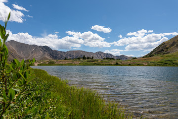 A beautiful lake, or tarn, with mountain peaks and puffy clouds in the background. A pretty view of...