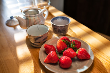 Closeup of traditional Japanese dessert strawberries on plate at wooden table in kitchen with two teacups or cups and teapot with green tea