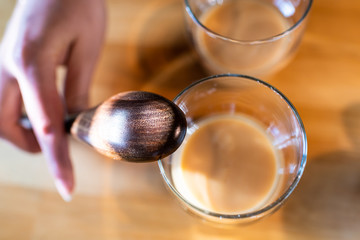 Flat top closeup view of two glasses with fermented Japanese traditional rice drink of amazake on kitchen wooden table with woman hand holding wood ladle spoon in Japan
