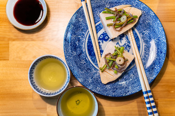 Traditional Japanese plate on wooden table with spring vegetable dish of takenoko bamboo shoots, sansai wild herbs with chopsticks, sencha green tea in cups and soy sauce