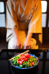 Young woman in kimono seiza sitting at traditional Japanese house or ryokan restaurant room by table with salad plates and chopsticks, shoji sliding paper doors
