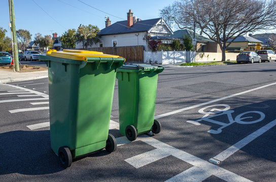 Two green household garbage bins placed on a clean suburban street with a view of some residential houses in distance. Melbourne, VIC Australia.