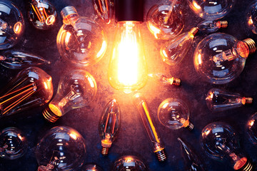 Vintage old light bulb glowing yellow on rough dark background surrounded by burnt out bulbs. Idea, creativity concept. © Leigh Prather