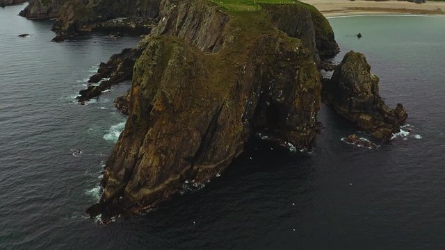 Aerial orbital view of epic cliffs and rockhouse near The Silver Strand beach in Ireland