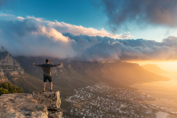 Young man standing on the edge at the top of Lion's head mountain in Cape Town with a beautiful...