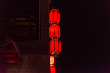 A string of cylindrical red lanterns hanging outside the walls of ancient buildings in Chinese New Year night