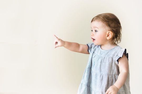 Baby girl pointing her finger, excited and emotional, on neutral background