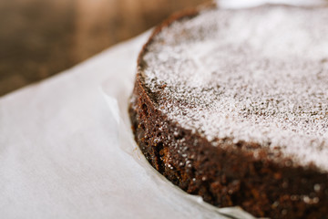 Traditional lumberjack fruit cake dusted with powdered sugar on parchment baking paper on wood surface