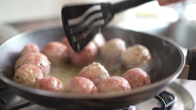 Succulent and tasty meatballs cooking in a pan in the kitchen of a house or in a restaurant. Stirring meatballs.